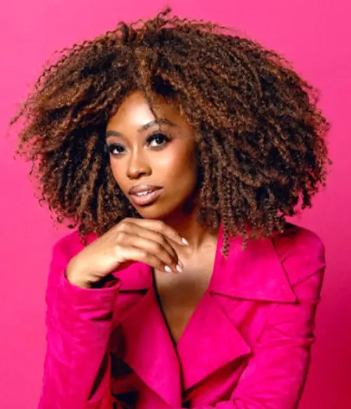 Woman with curly hair wearing a pink jacket against pink background