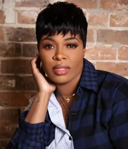 Woman with short black hairstyle and plaid shirt in front of brick wall